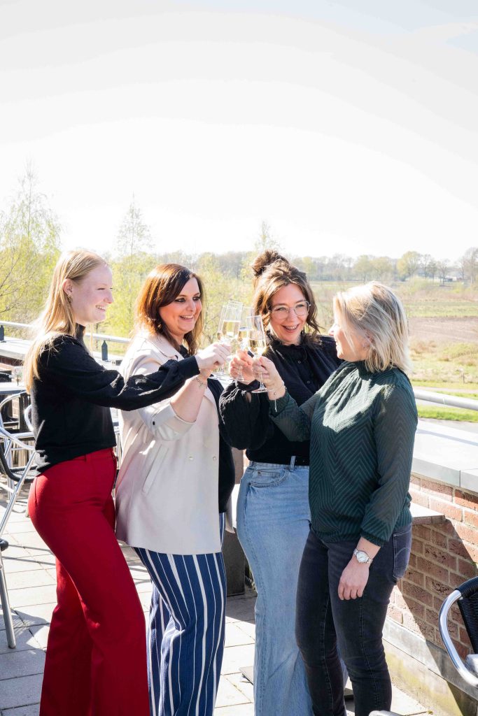 Vier vrouwen proosten met champagne op terras.