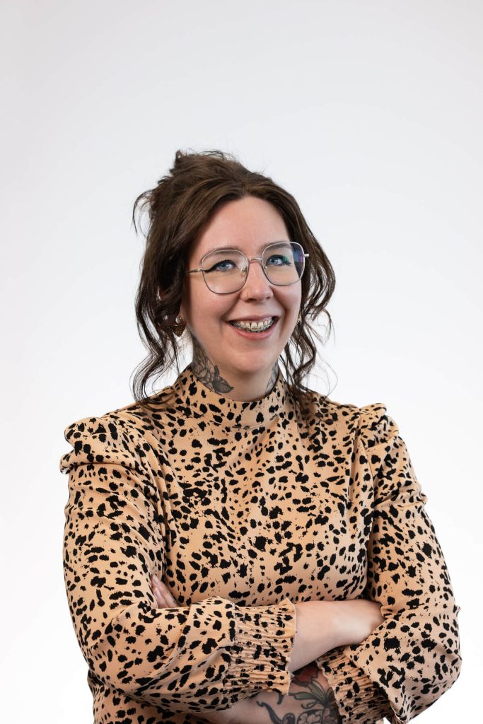 Vrouw in gevlekte jurk met bril en tattoos.
